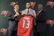 Tampa Bay Buccaneers first-round draft pick Mike Evans, center, holds up his jersey with general manager Jason Licht, left, and head coach Lovie Smith, right, after a news conference Friday, May 9, 2014, in Tampa, Fla. Evans, a wide receiver from Texas A&M, was the seventh player chosen. (AP Photo/Chris O'Meara)