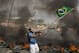 A member of the Homeless Workers Movement waves a Brazilian flag by burning tires during a protest against the money spent on the World Cup near Itaquerao stadium, behind, which will host the international soccer tournament's first match in Sao Paulo, Brazil, Thursday, May 15, 2014. Brazilians are angry at the billions spent to host the World Cup, much of it on 12 ornate football stadiums, one-third of which critics say will see little use after the big event. (AP Photo/Andre Penner)