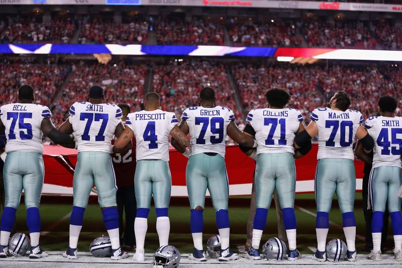 GLENDALE, AZ - SEPTEMBER 25: Quarterback Dak Prescott #4 of the Dallas Cowboys links arms with teammates offensive tackle Tyron Smith #77 and offensive guard Chaz Green #79 during the National Anthem before the start of the NFL game against the Arizona Ca
