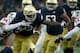 SOUTH BEND, IN - OCTOBER 28: Josh Adams #33 of the Notre Dame Fighting Irish runs with the ball while being tackled by Tim Kidd-Glbad #34 and Shawn Boone #24 of the North Carolina State Wolfpack in the second quarter at Notre Dame Stadium on October 28,