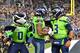 SEATTLE, WASHINGTON - DECEMBER 02: Russell Wilson #3 of the Seattle Seahawks, right, and mascot Blitz, left, congratulate Rashaad Penny #20, center, after scoring a touchdown during the game against the Minnesota Vikings at CenturyLink Field on December 0