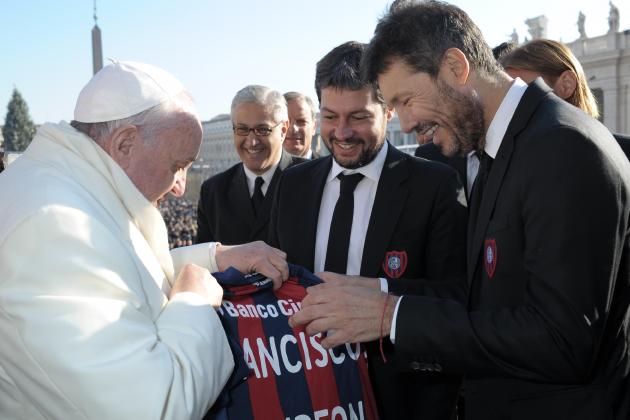 In this picture provided by the Vatican newspaper L'Osservatore Romano, Pope Francis is presented with a jersey of San Lorenzo soccer team by team's President Matias Lammens, right, and deputy-president Marcelo Tinelli, center, at the Vatican, Wednesday, Dec. 18, 2013. Pope Francis has celebrated his beloved San Lorenzo's victory in the Argentine soccer championship, hoisting up their trophy for all to see. A small group of team managers and players met with Francis on the steps of St. Peter's Basilica at the end of his Wednesday general audience. The group presented him with the trophy and a red and blue team jersey with