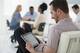 A fresh white building interior, flooded with light. A group of people meeting. One person seated separately, using a tablet computer. (Mint Images/AP Images).
