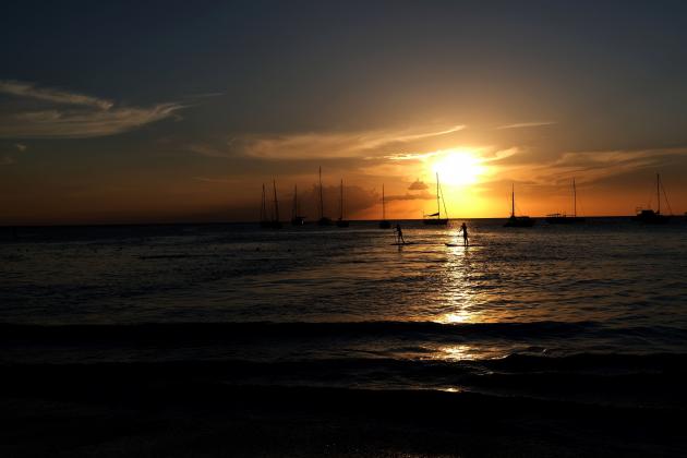Two tourists sail on paddle board on the water along a beach as the sun sets in Bridgetown, Barbados, on March 24, 2017. / AFP PHOTO / Jewel SAMAD        (Photo credit should read JEWEL SAMAD/AFP/Getty Images)