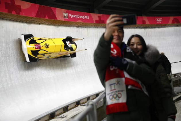 Driver Nico Walther and Christian Poser of Germany pass a couple as they pose for a selfie during the two-man bobsled competition at the 2018 Winter Olympics in Pyeongchang, South Korea, Sunday, Feb. 18, 2018. (AP Photo/Patrick Semansky)