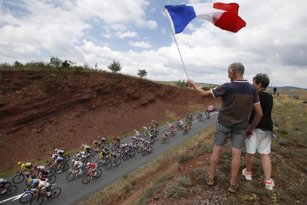 Spectators wave the French flag as the pack with Britain's Geraint Thomas, wearing the overall leader's yellow jersey, bottom left, passes during the fifteenth stage of the Tour de France cycling race over 181.5 kilometers (112.8 miles) with start in Millau and finish in Carcassonne, France, France, Sunday July 22, 2018. (AP Photo/Christophe Ena )