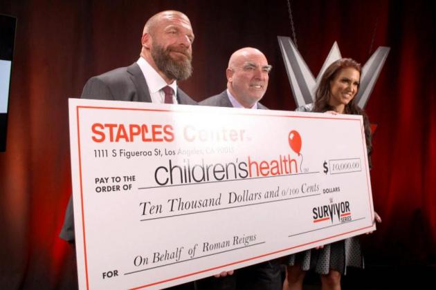 Triple H, Lee Zeldman and Stephanie McMahon holding a check donated to "Children's Health" on behalf of Roman Reigns.
