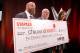 Triple H, Lee Zeldman and Stephanie McMahon holding a check donated to "Children's Health" on behalf of Roman Reigns.