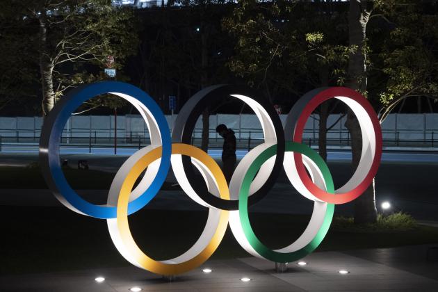 A man is seen through the Olympic rings in front of the New National Stadium in Tokyo, Tuesday, March 24, 2020. IOC President Thomas Bach has agreed