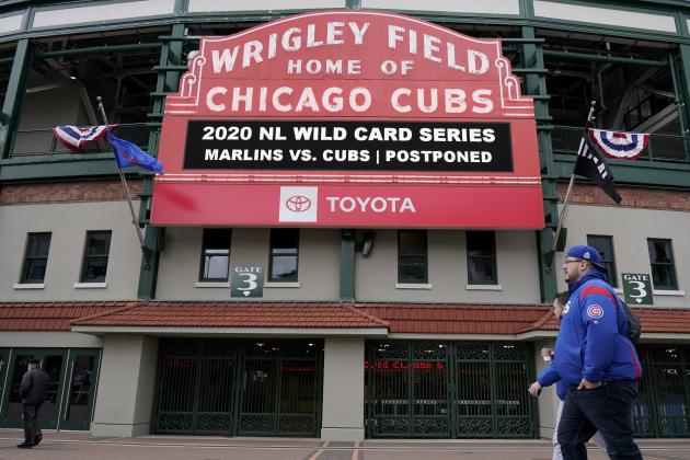 People walk by the front of Wrigley Field where the marquee advises that today's Game 2 of a National League wild-card baseball series between the Miami Marlins and Chicago Cubs has been postponed in Chicago, Thursday, Oct. 1, 2020. The game that was postponed due to weather is scheduled to be played Friday. (AP Photo/Nam Y. Huh)