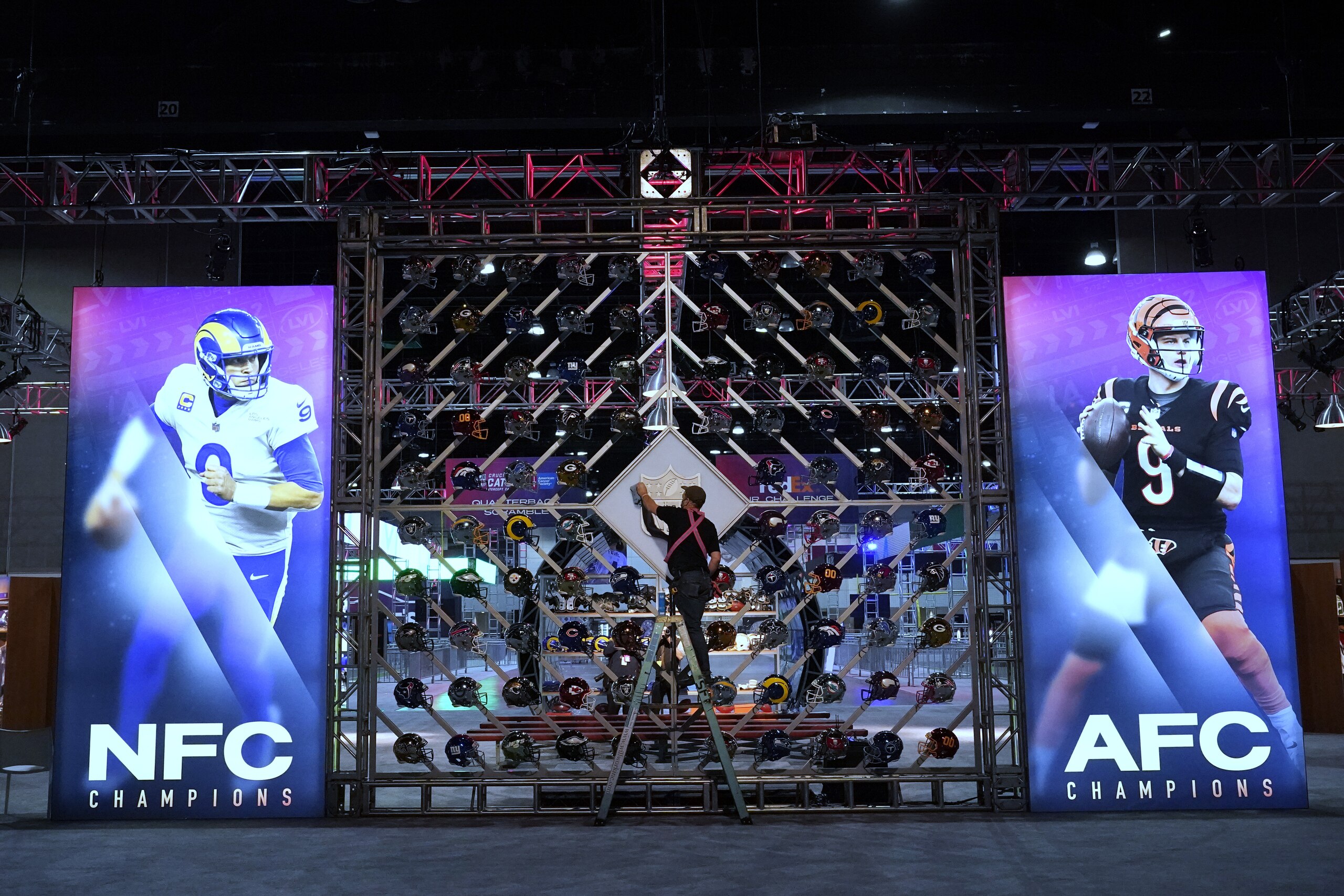 A worker cleans a league logo between images of Los Angeles Rams quarterback Matthew Stafford, left, and Cincinnati Bengals quarterback Joe Burrow inside the NFL Experience, an interactive fan show, Friday, Feb. 4, 2022, at the Los Angeles Convention Center in Los Angeles. The Los Angeles Rams play the Cincinnati Bengals in the Super Bowl NFL football game on Sunday, Feb. 13. in Inglewood, Calif. (AP Photo/Marcio Jose Sanchez)